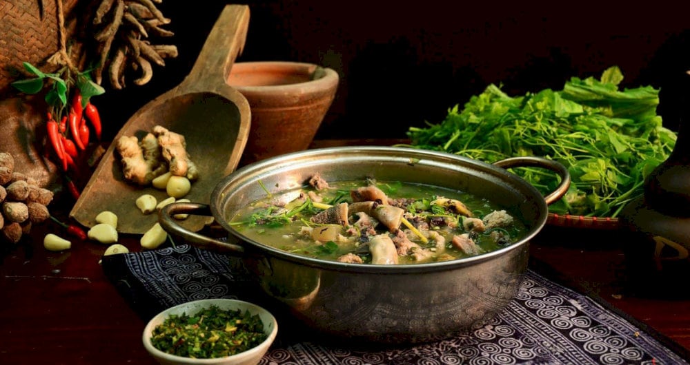 A steaming pot of Thang Co bubbling over firewood, served with fresh greens and maize wine